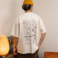 Person wearing a beige t-shirt with 'Big Dog Coffee' graphic design, standing in a room with a lamp and furniture.