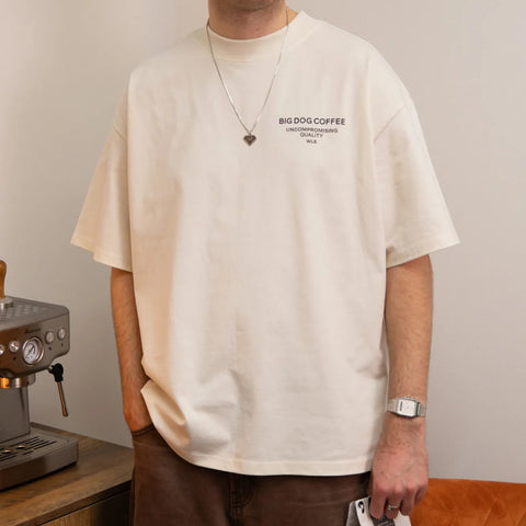 Person wearing a beige t-shirt with 'BIG DOG COFFEE' text, standing next to a coffee machine.
