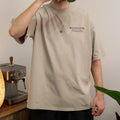 Person wearing a beige t-shirt with 'Big Dog Coffee Speciality Coffee for Everyday People', standing in a kitchen.